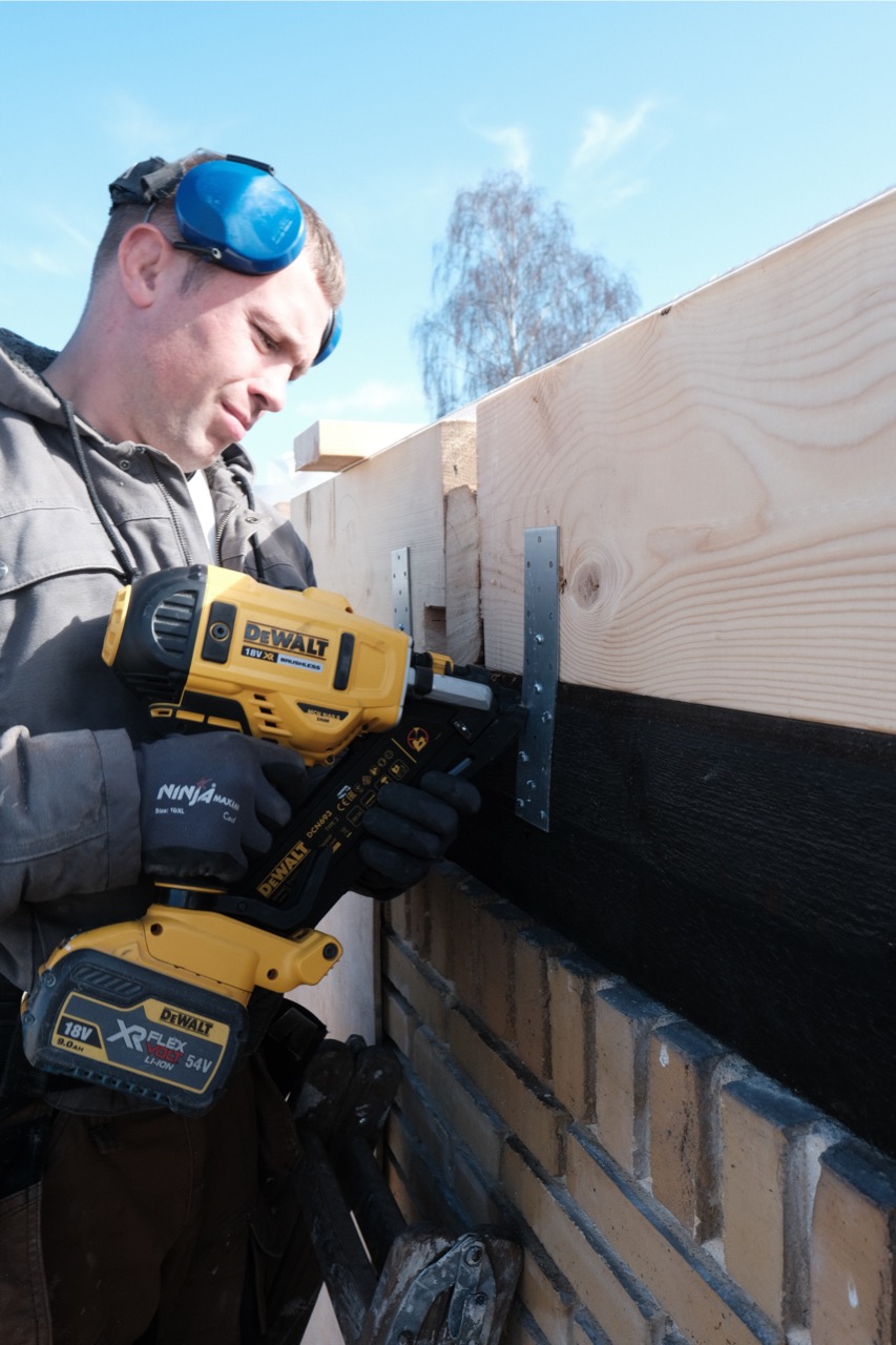 A construction worker fastening timber above a brick wall